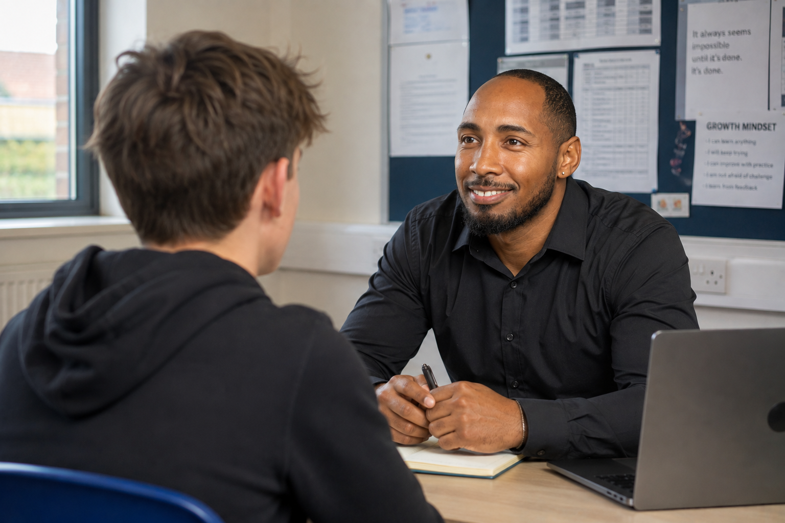 A mentor talking with a teenage student across a desk in a school classroom